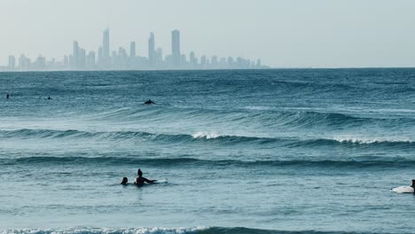 surfers riding waves with distant city skyline