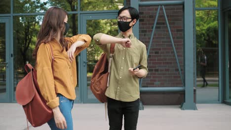 estudiante asiático con mascarilla protectora saludando con el codo a sus compañeros de clase en la calle cerca de la universidad