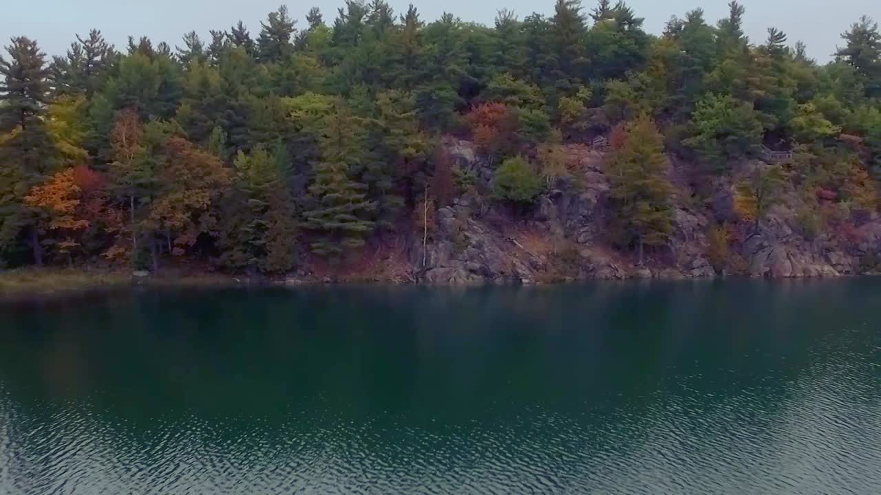 Backwards aerial tracking shot of Pink Lake at Gatineau Park during ...