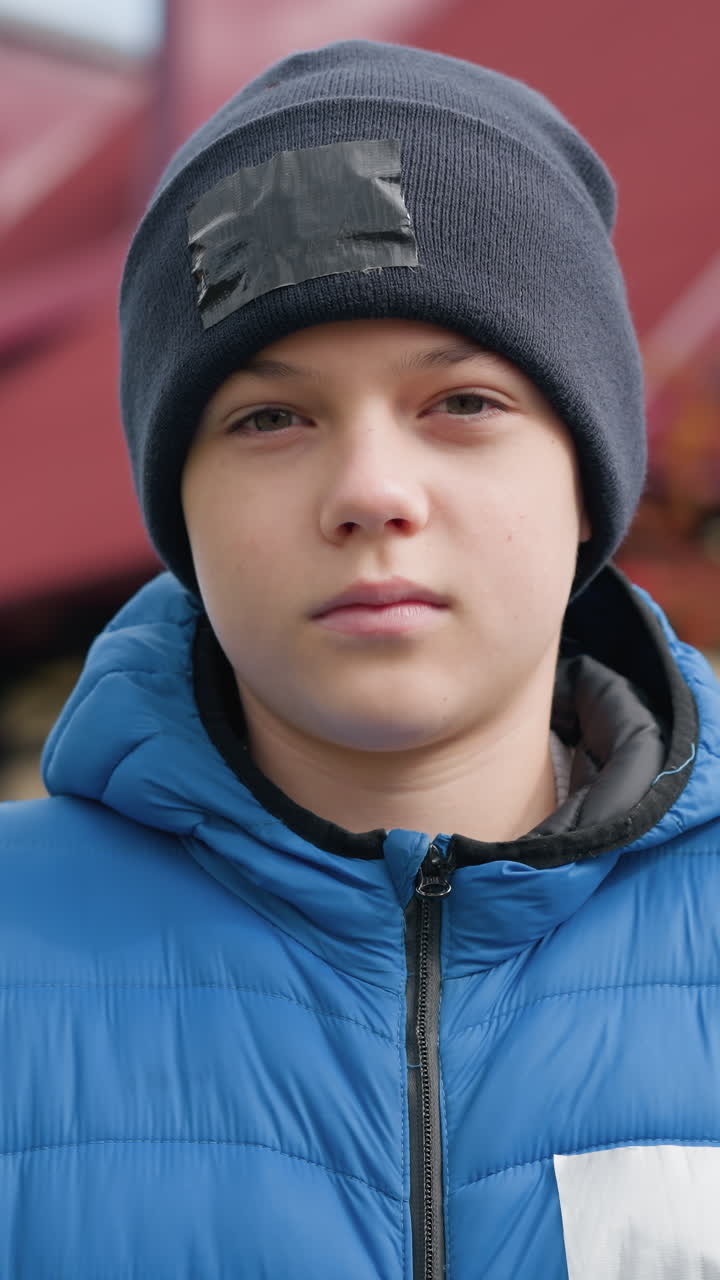 niño con gorra negra y chaqueta azul de pie al aire libre, mirando pensativo frente a hermosos árboles de otoño con hojas rojas coloridas y una casa en el fondo
