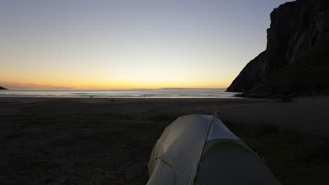 toma fija de la carpa de los campistas frente a la tranquila puesta de sol en la playa de kvalvika, noruega