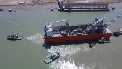 Aerial-view-of-cargo-ship-arriving-at-the-port-with-the-help-of-tugs