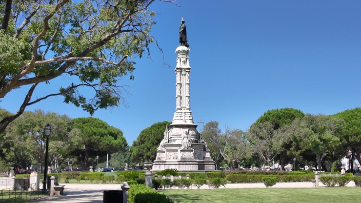 Monumento ad Afonso de Albuquerque a Lisbona, Portogallo, incorniciato da alberi e cielo azzurro brillante.