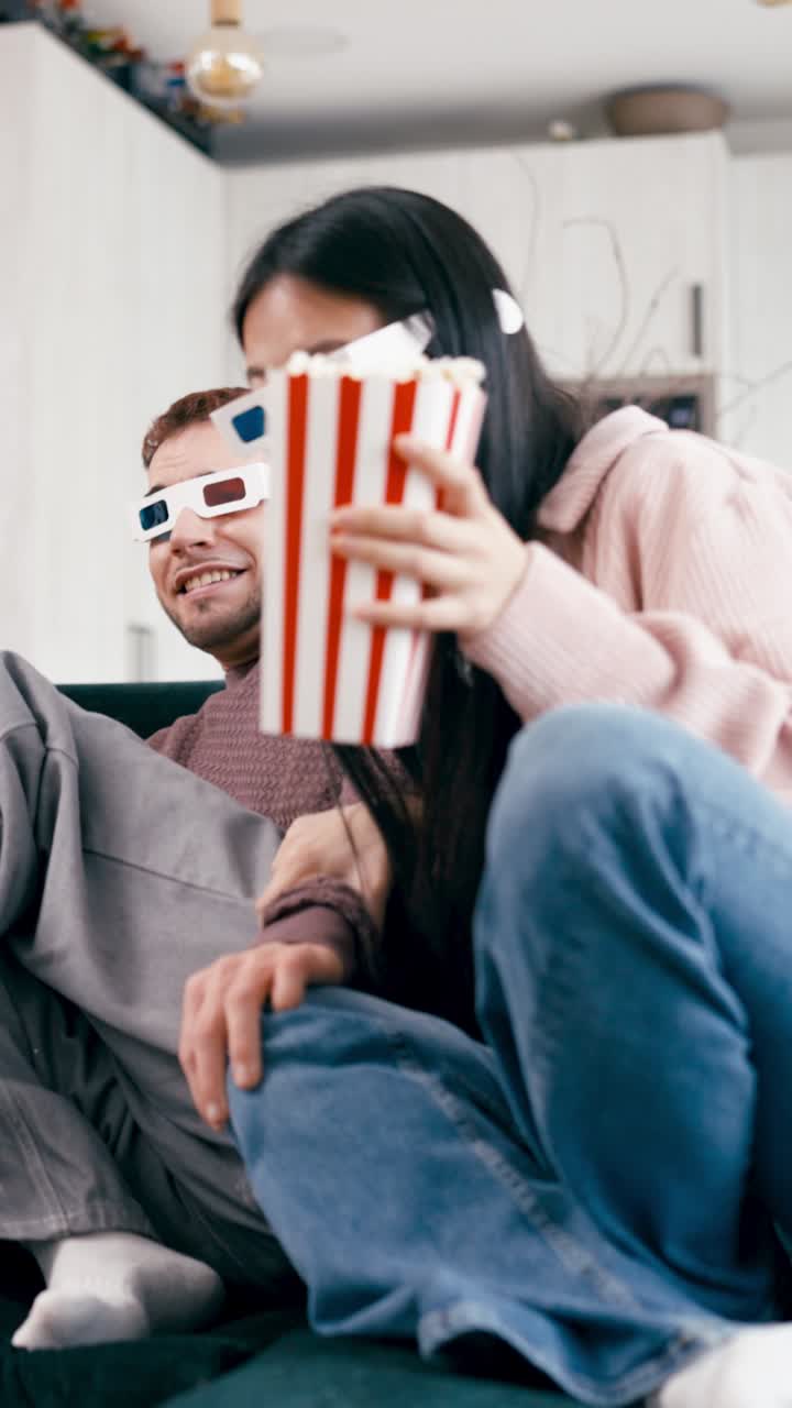 Casal usando óculos 3D assistindo a um filme e comendo pipoca em casa