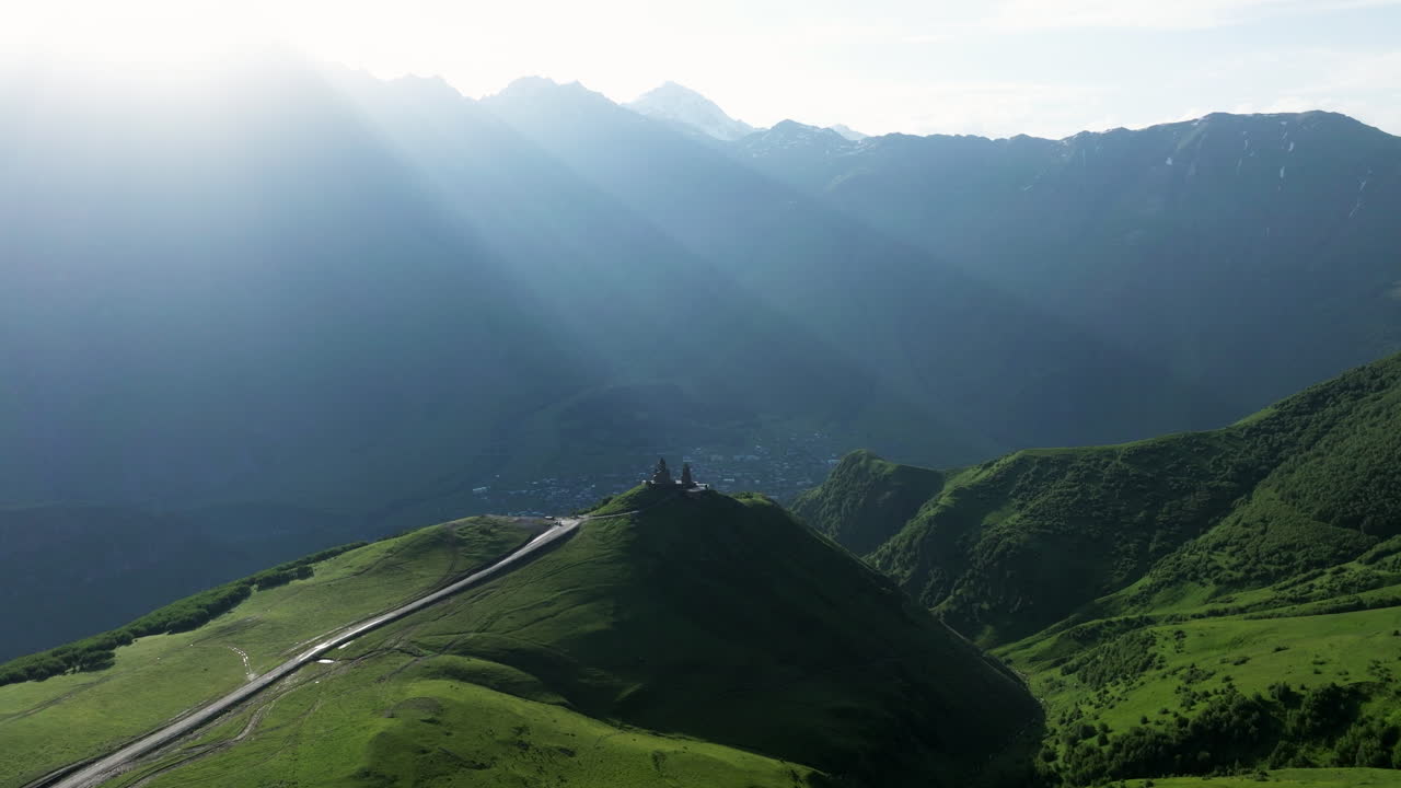 el sol brilla sobre la pintoresca cordillera y la iglesia de la trinidad gergeti en kazbegi, georgia