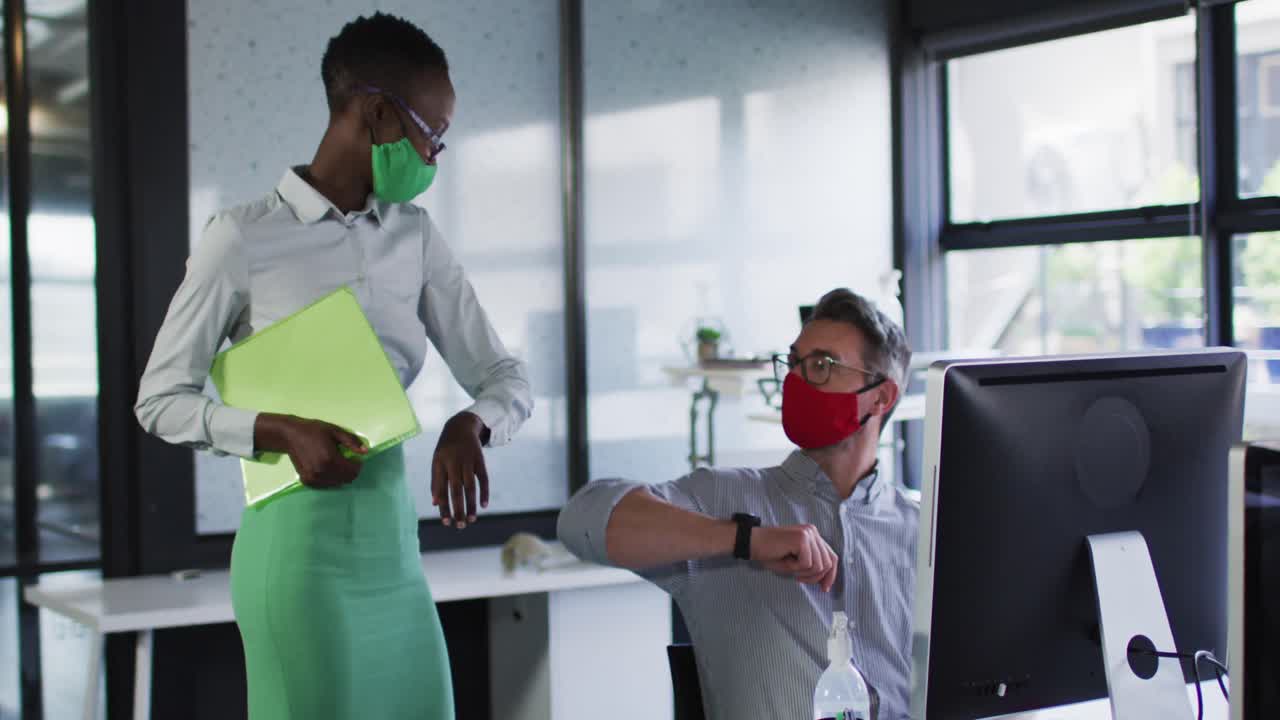 Diverse male and female office colleagues wearing face masks greeting each other by touching elbows