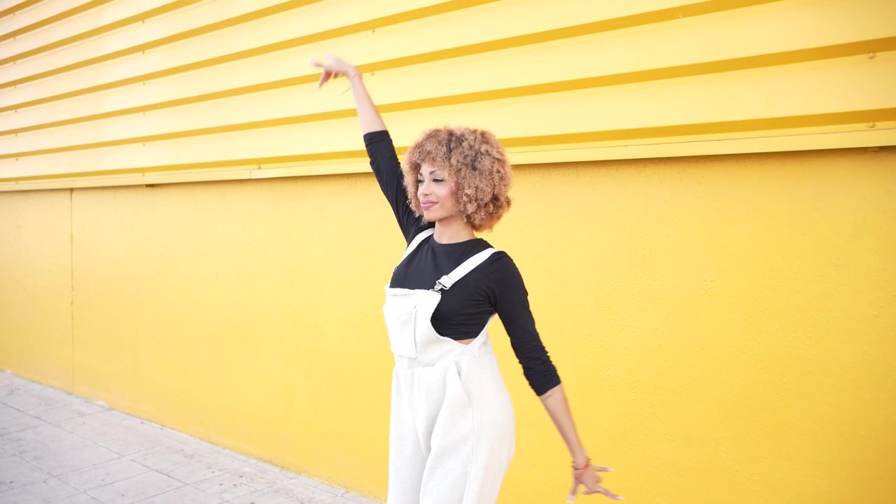 A fashionable young woman joyfully dancing playfully against a bright yellow wall