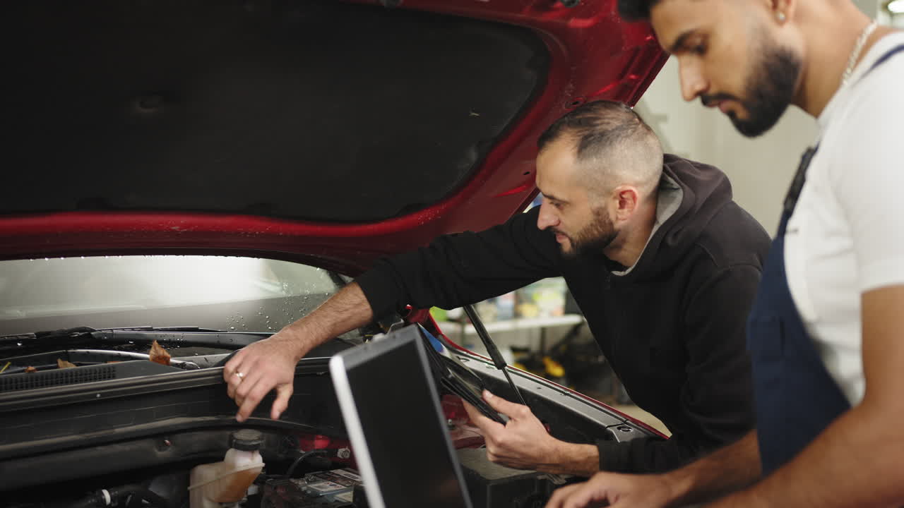 mecánicos de automóviles inspeccionando un automóvil rojo bajo el capó con herramientas de diagnóstico