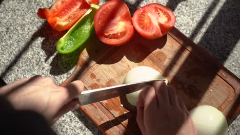 slicing white onion on cutting board with tomatoes and bell pepper on the side