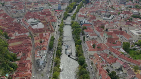 High-scenic-reverse-aerial-view-above-Graz-city-orange-rooftops-Austria-following-Mur-river-Murinsel-artificial-island-landmark