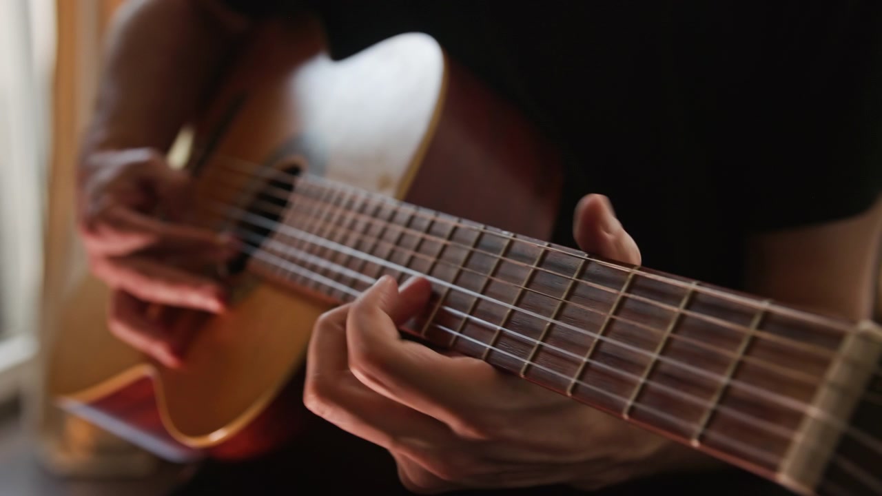 Zbliżenie na osobę grającą na akustycznej gitarze klasycznej, wykonującą solo w zwolnionym tempie techniką fingerstyle. Wideo charakteryzuje się pięknym, realistycznym, ciepłym oświetleniem i wysoką jakością estetyki wizualnej.