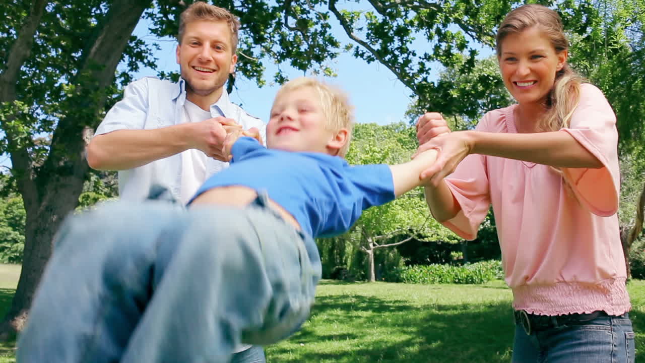 두 부모 는 아들 의 팔 을 잡고 놀이 로 앞뒤로 흔들면서 미소 짓고 있다