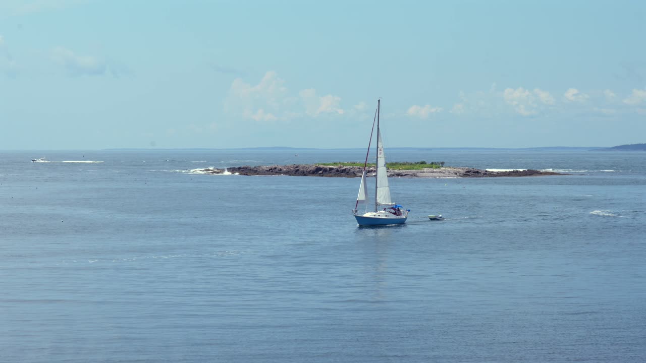 A sailboat sailing into the harbor pulling a small dinghy at Monhegan Island in Maine.