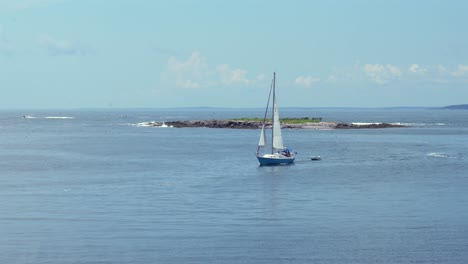 a sailboat sailing into the harbor pulling a small dinghy at monhegan island in maine.