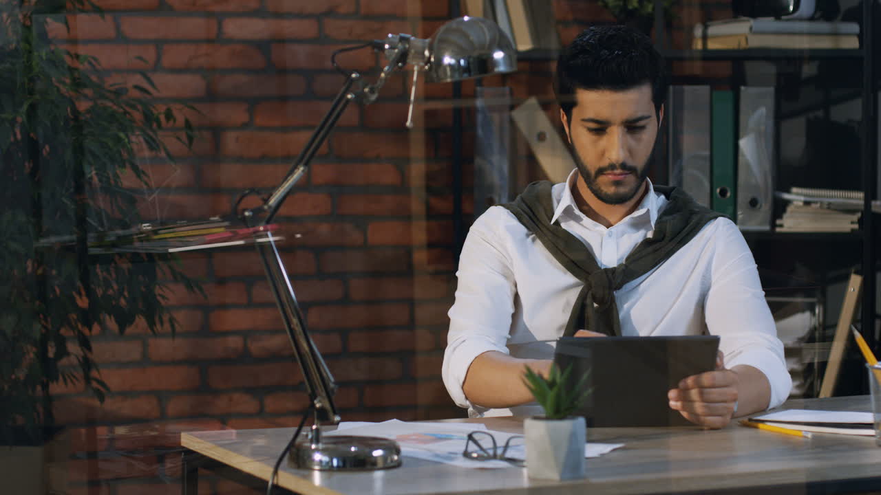 Good Looking Arabian Businessman Taping And Typing On The Tablet While Sitting At Desk In The Office