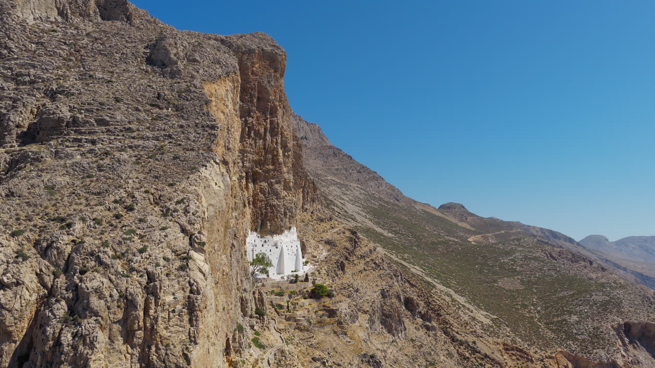 Hozoviotissa Monastery on rocky cliffside above sea, Amorgos Island, Greece, tracking right reveal past cliff edge