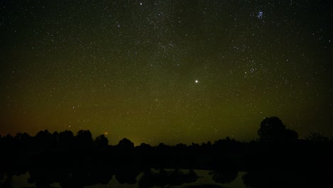 colorful starry sky over the forest in nature landscape. light pollution in the sky from a city lights far away. mild aurora borealis in green colors. sky timelapse full of stars.
