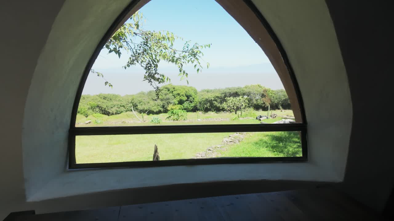 Unique window view from inside an earthen home, showing a narrow hallway with natural light pouring over table overlooking grassy field