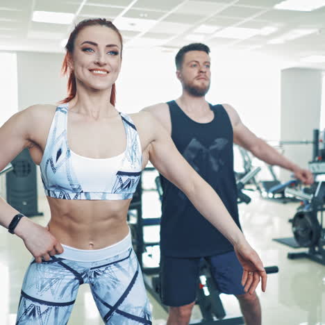 Smiling couple doing workout in fitness club. Beautiful female trainer shows different exercises to a man in front of the mirror at gym indoors.