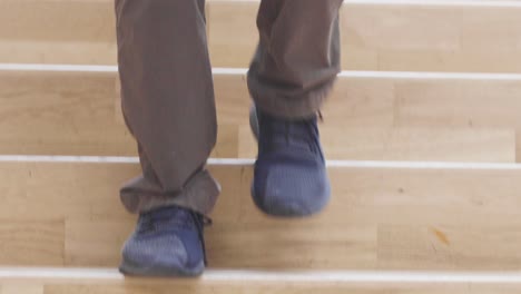 close up of a male walking down a broad wooden modern staircase with dark shoes and jeans on