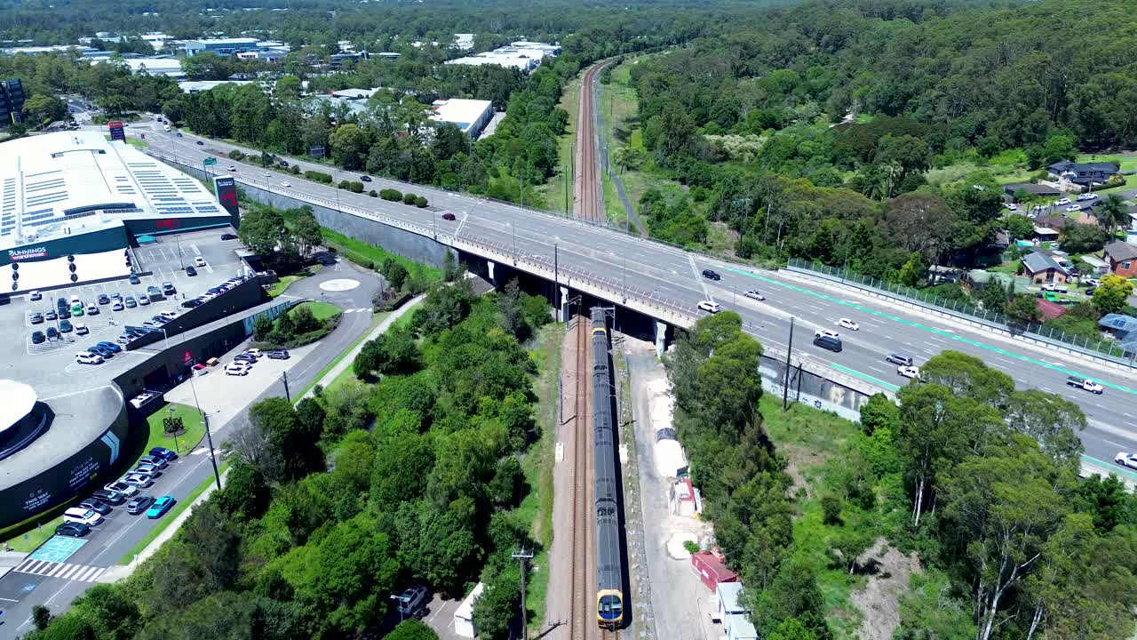 Drone aerial landscape of commuter train on railway tracks at underpass Tuggerah bridge station platform with car vehicles transport Central Coast Australia urban infrastructure travel