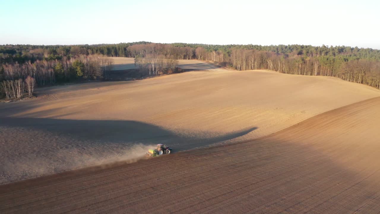 Traktor arbeider på en jordbruksplantasje ved solnedgang
