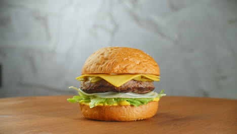 Gran-Hamburguesa-Con-Chuleta-De-Ternera,-Tomates,-Champiñones-Y-Pepinos-Con-Queso-Derretido-Gira-Sobre-Una-Tabla-De-Madera-Sobre-Un-Fondo-Claro.