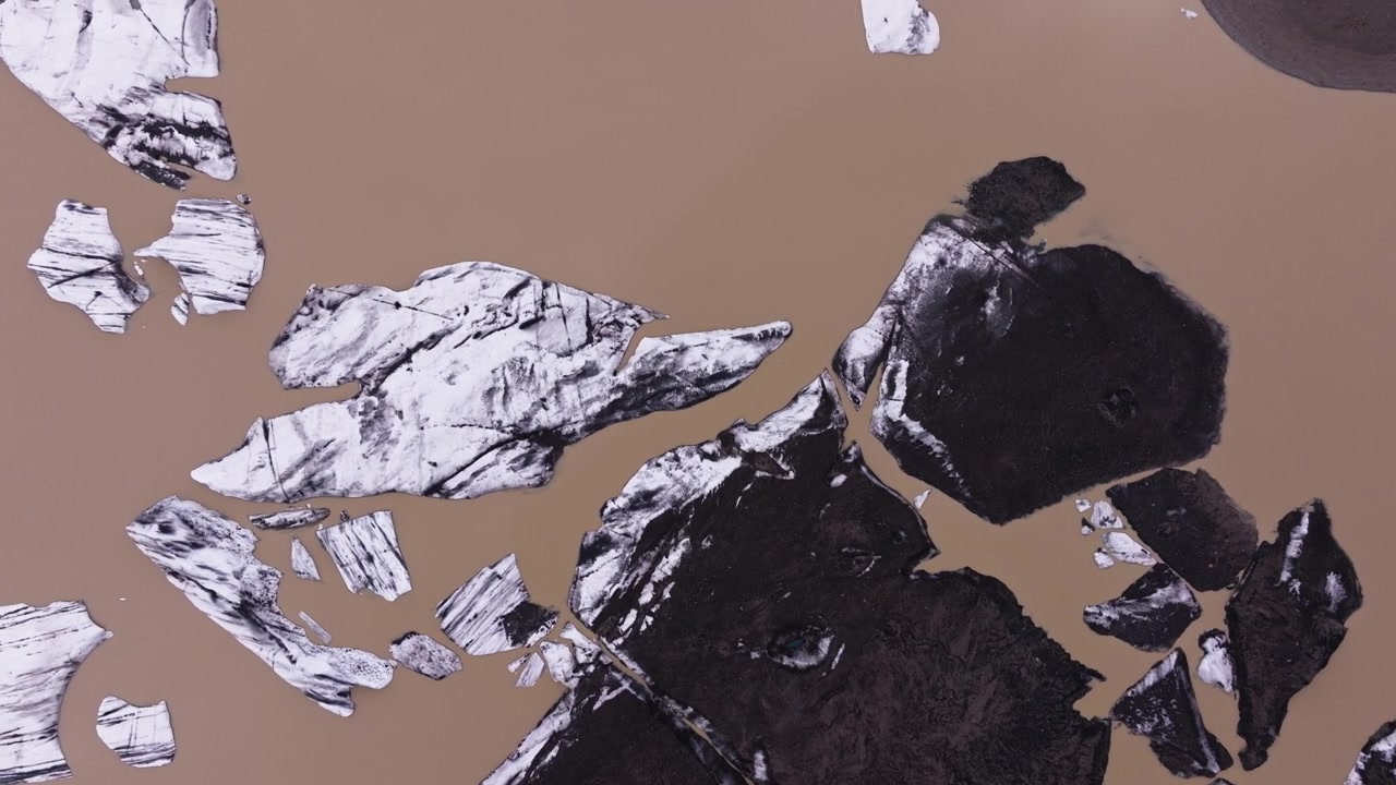 Aerial view of glacier ice fragments floating on muddy water in remote Icelandic landscape