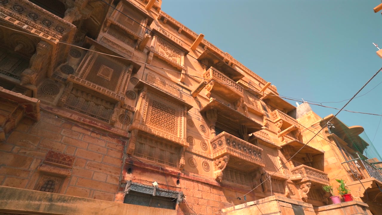 Toma estática cinematográfica en ángulo contrapicado de balcones de arenisca intrincadamente tallados y ventanas jaali en una haveli tradicional en Jaisalmer, Rajastán, India
