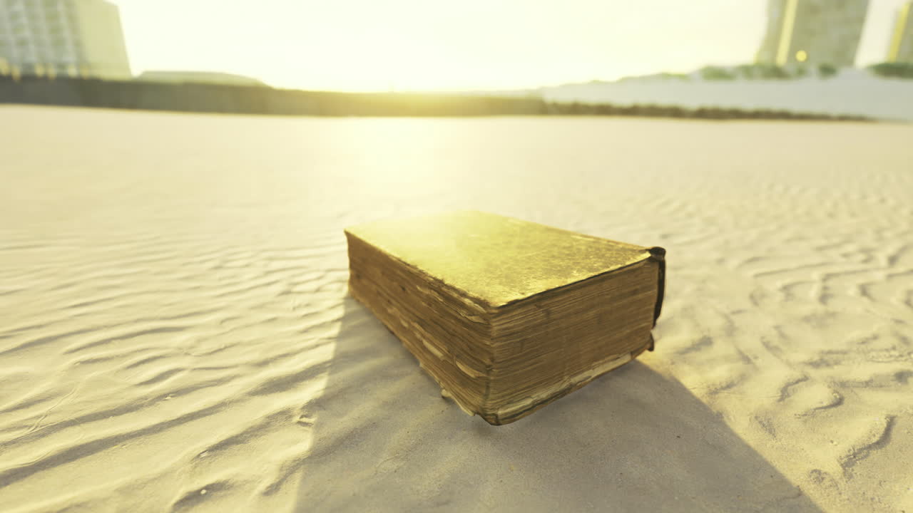 Sunset light shines on an old book resting on sandy beach surface