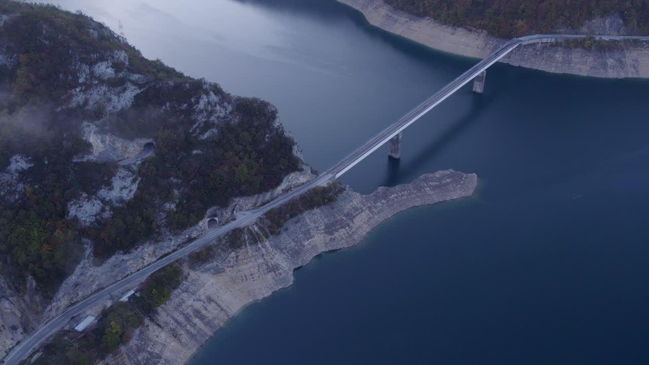 Ilmakuva majesteettisesta sillasta Piva-järven yli vuoristoisessa kanjonissa auringonnousun aikaan Plužinessa, Montenegrossa. Upea auringonnousun valaistus, rauhallinen tunnelma, korkealaatuinen dronekuvaus paljastaa rauhallisen maiseman.