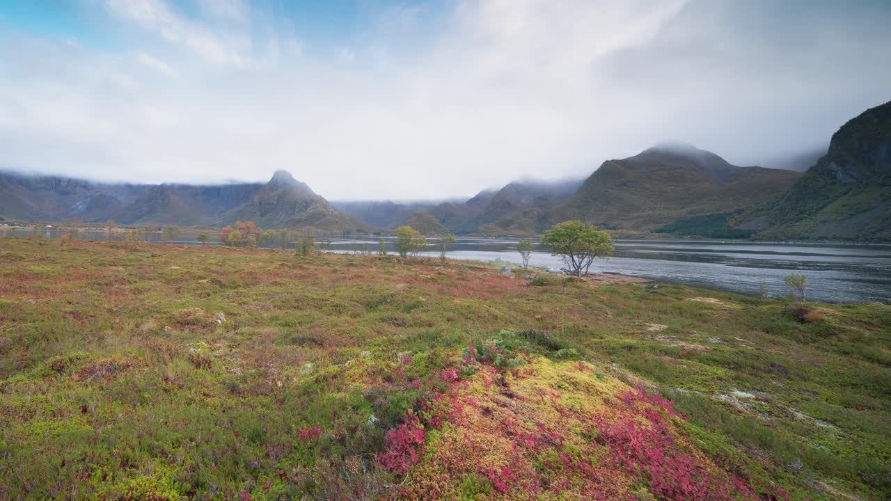 Lage wolken wervelen en trekken voorbij boven de fjord en herfstvallei, omringd door bergen, in een timelapsevideo