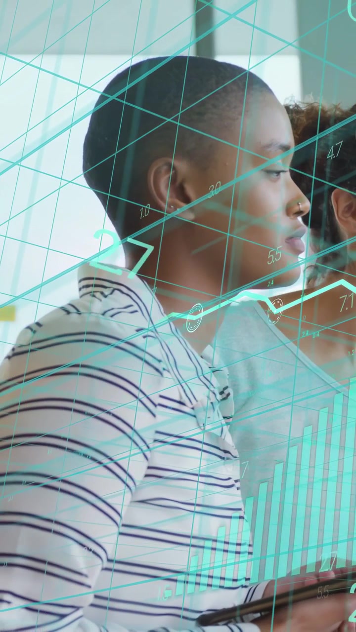 Vertical video: Striped woman holding tablet assessing data as teal charts sweeping in tech office