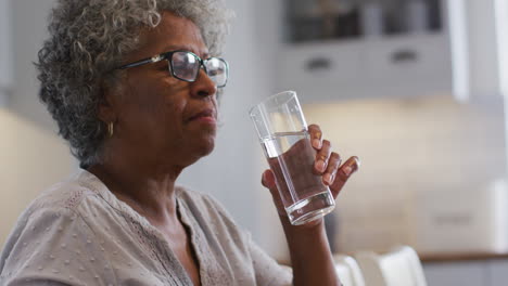 senior african american woman taking medication and drinking water while sitting at home