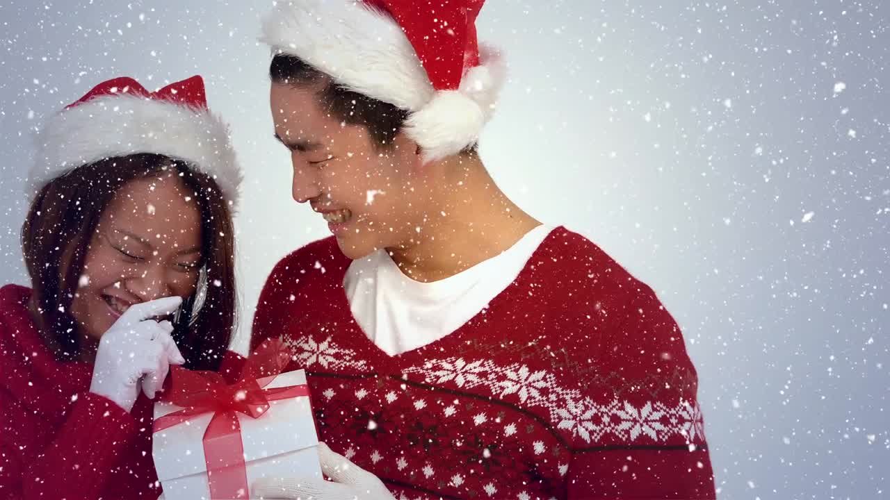 composición de video con nieve cayendo sobre pareja feliz con regalo