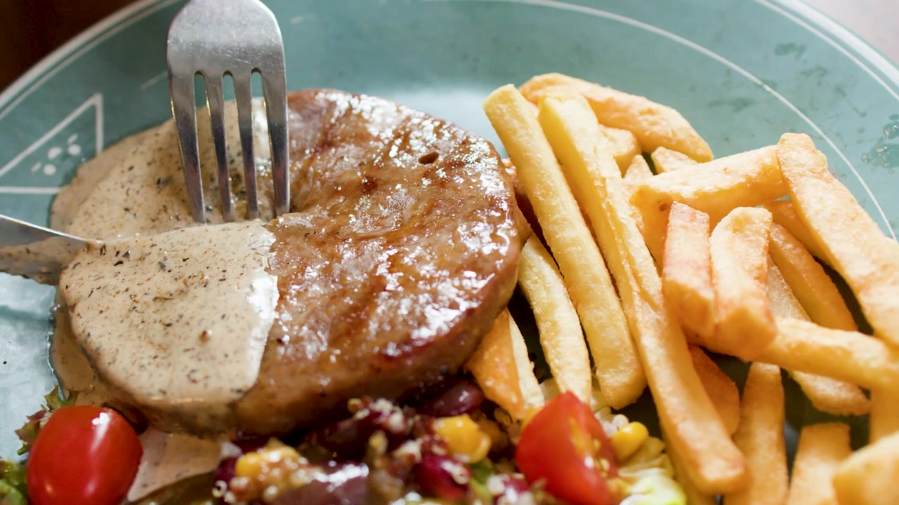Primo piano di un coltello e una forchetta che tagliano una bistecca alla griglia servita con salsa