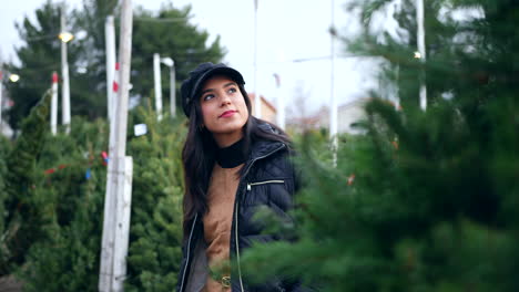 una mujer hermosa con un espíritu navideño feliz sonriendo mientras compra árboles de navidad festivos de abeto douglas