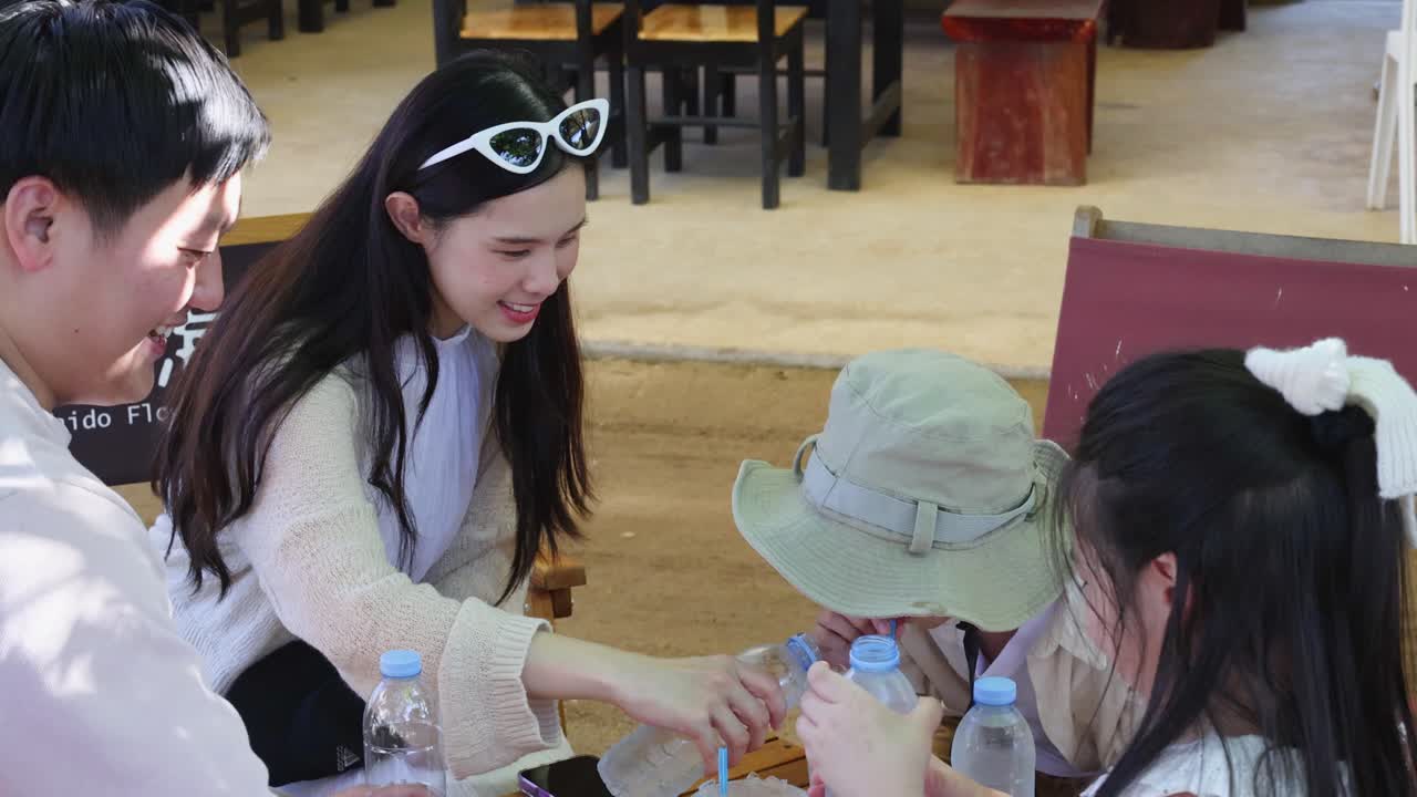 晴れた日の屋外カフェのテーブルで、ボトルウォーターを分け合いながら、親と子供たちが一緒に笑っています。