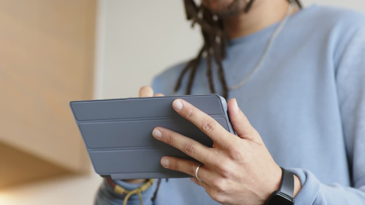 Man is tilting slim tablet, opening cover, swiping screen and browsing content in home office