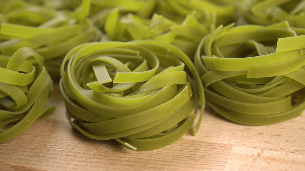 Raw green uncooked nests pasta tagliatelle on a wooden surface