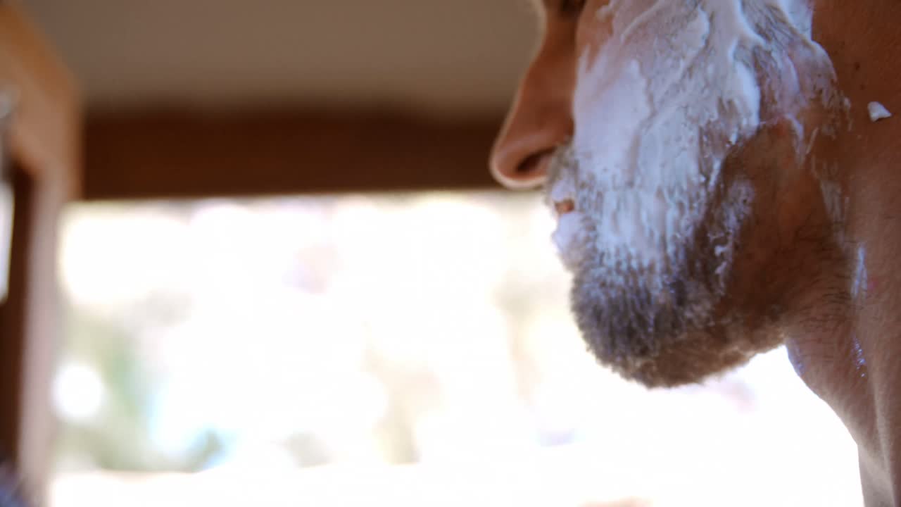 hombre afeitando su barba con una navaja de afeitar en la cabaña 4k