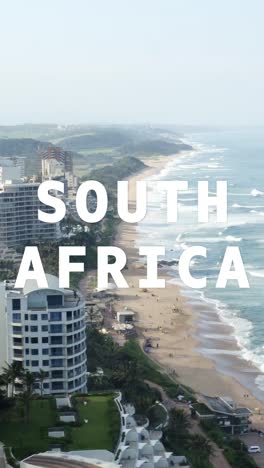 Vertical-Video-Drone-Shot-Of-Coastline-With-Ocean-And-Beach-Resort-Overlaid-With-Graphic-Spelling-Out-South-Africa