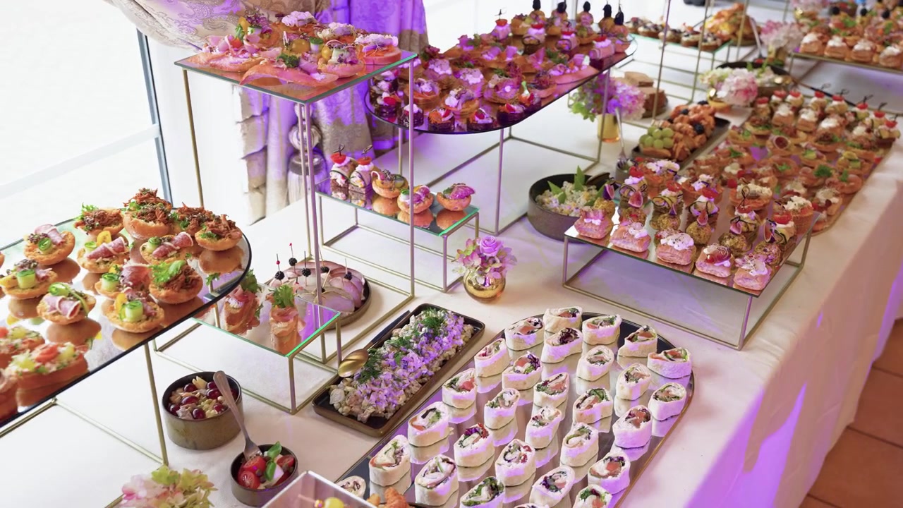 Et elegant festbord fyldt med et udvalg af gourmet-forretter, kager og desserter, smukt arrangeret på fade i flere niveauer i klart naturligt lys, perfekt til arrangementer