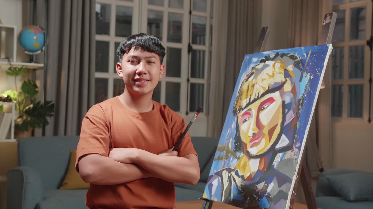 Asian Artist Boy Holding Paintbrush Mixed Colour, Crossing His Arm, And Smiling After Finish Painting A Girl On The Canvas