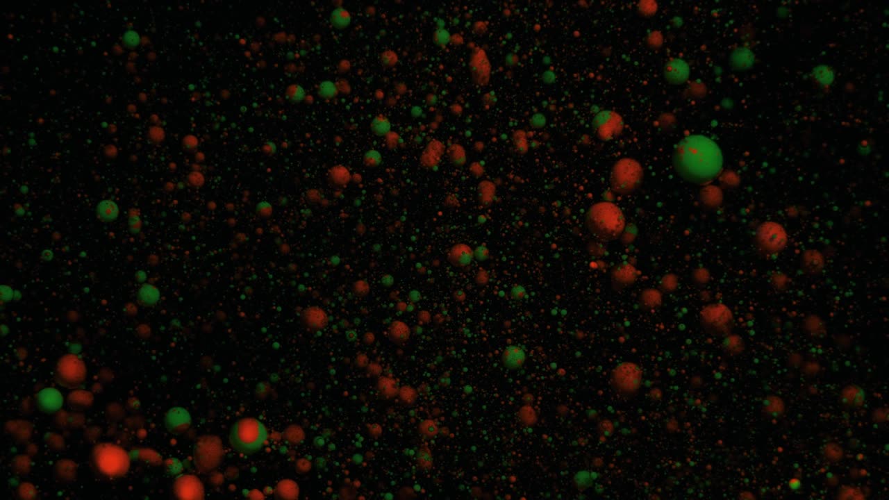 Orange and green volumetric fluorescent particles move and change on a black moving background, transition.
