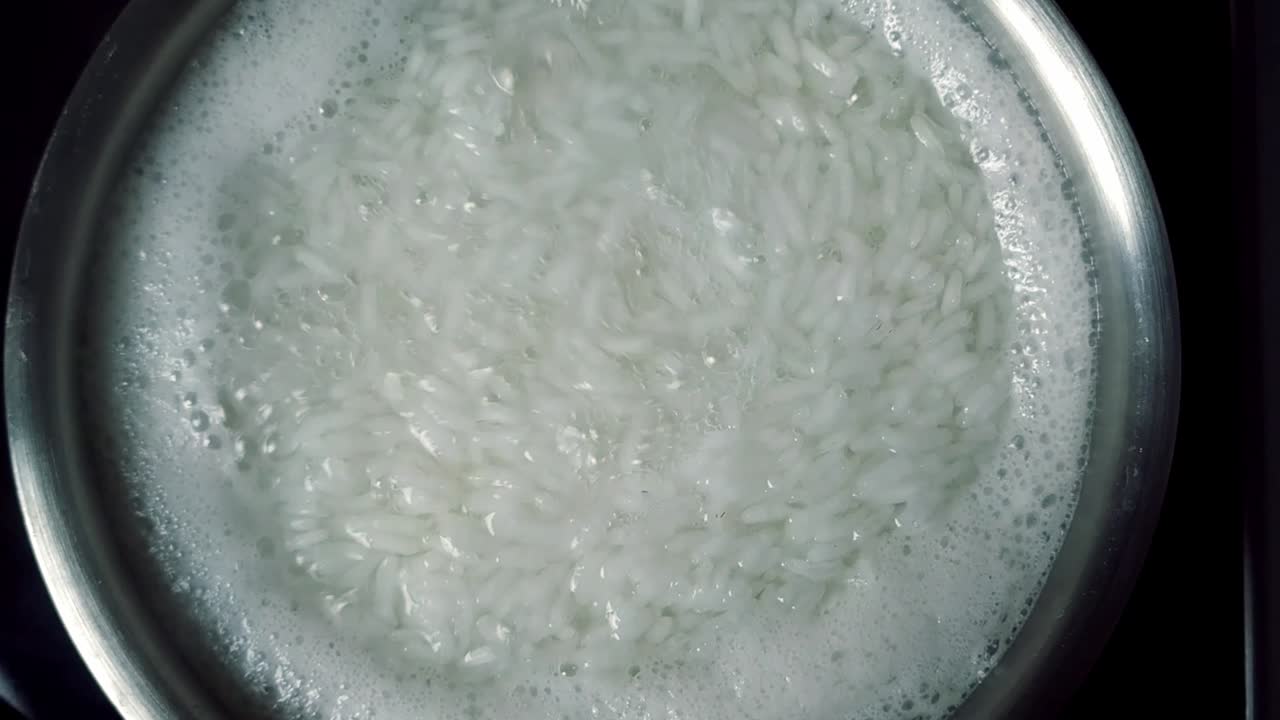 Riso bianco che bolle con vapore in un recipiente d'acciaio, primo piano.
