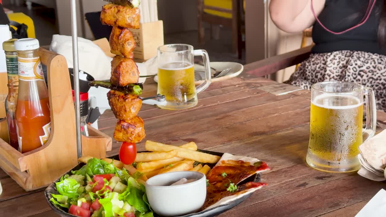 Casual dining scene with skewers, fries, and beer at a beach club in Phuket, Thailand. Bright, relaxed atmosphere