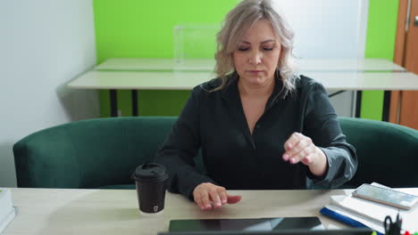 focused freelancer prepares for productive work session, opening laptop on organized desk with takeaway coffee cup, smartphone, notebooks, and colorful pens in bright, modern workspace