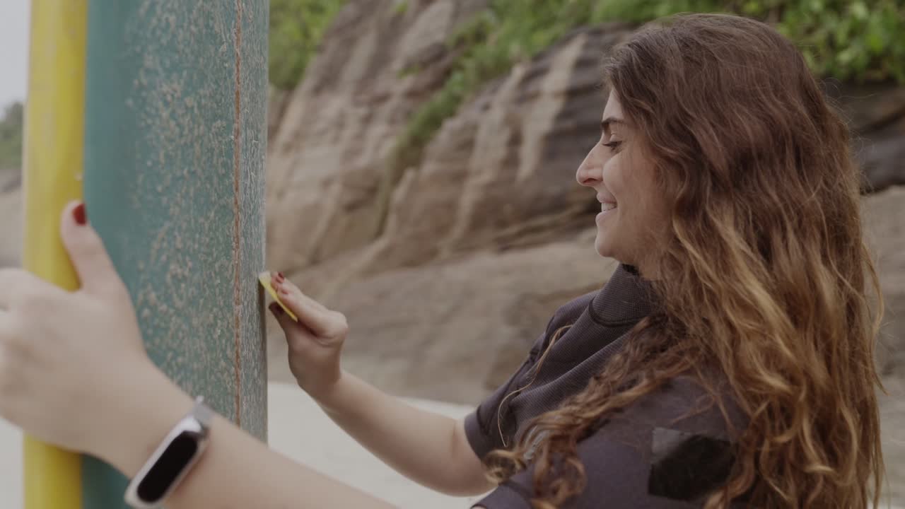 Woman Waxing a Surfboard on the Beach