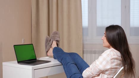 young woman throwing her legs on the table, looking at a laptop with a green screen